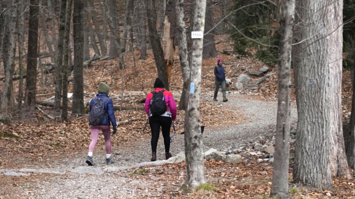 Two hikers head up a trailhead of Great Blue Hill, while one completes her hike from the summit, at the Blue Hills Reservation, Wednesday, Dec. 28, 2022, in Milton, Mass. First Day Hikes, that started in Massachusetts in 1992, have become a nationwide phenomenon. Thousands of people are expected to take part in First Day Hikes at hundreds of state parks in all 50 states this New Year's Day.