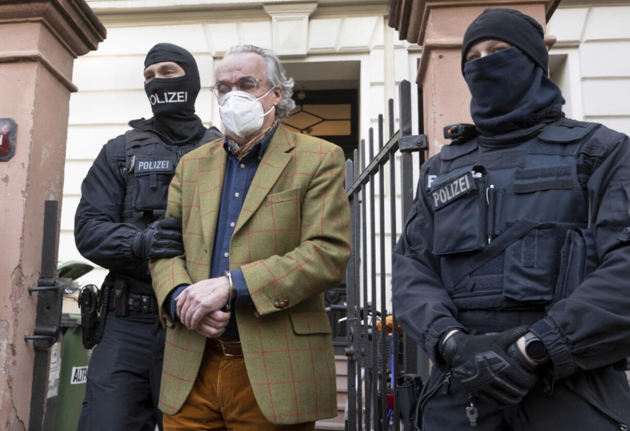 Masked police officers lead Heinrich XIII Prince Reuss, center, to a police vehicle during a raid against so-called 'Reich citizens' in Frankfurt, Germany, Wednesday, Dec. 7, 2022. Thousands of police carried out a series of raids across much of Germany on Wednesday against suspected far-right extremists who allegedly sought to overthrow the state by force. Federal prosecutors said some 3,000 officers conducted searches at 130 sites in 11 of Germany's 16 states against adherents of the so-called Reich Citizens movement. Some members of the grouping reject Germany's postwar constitution and have called for the overthrow of the government.