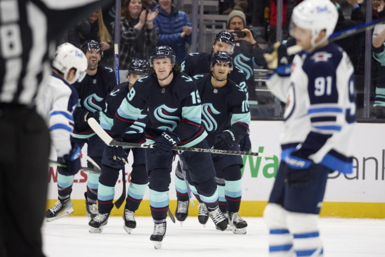 Seattle Kraken left wing Jared McCann (19) leads the team to the bench while celebrating after his goal against the Winnipeg Jets during the third period of an NHL hockey game, Sunday, Dec. 18, 2022, in Seattle.