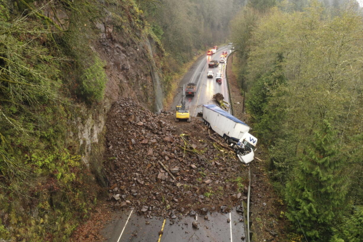 In this photo provided by the Oregon Department of Transportation, crews work to clear debris and remove a disabled truck on U.S. 30 east of Astoria, Ore., Wednesday, Nov. 30, 2022, after a landslide Tuesday night.