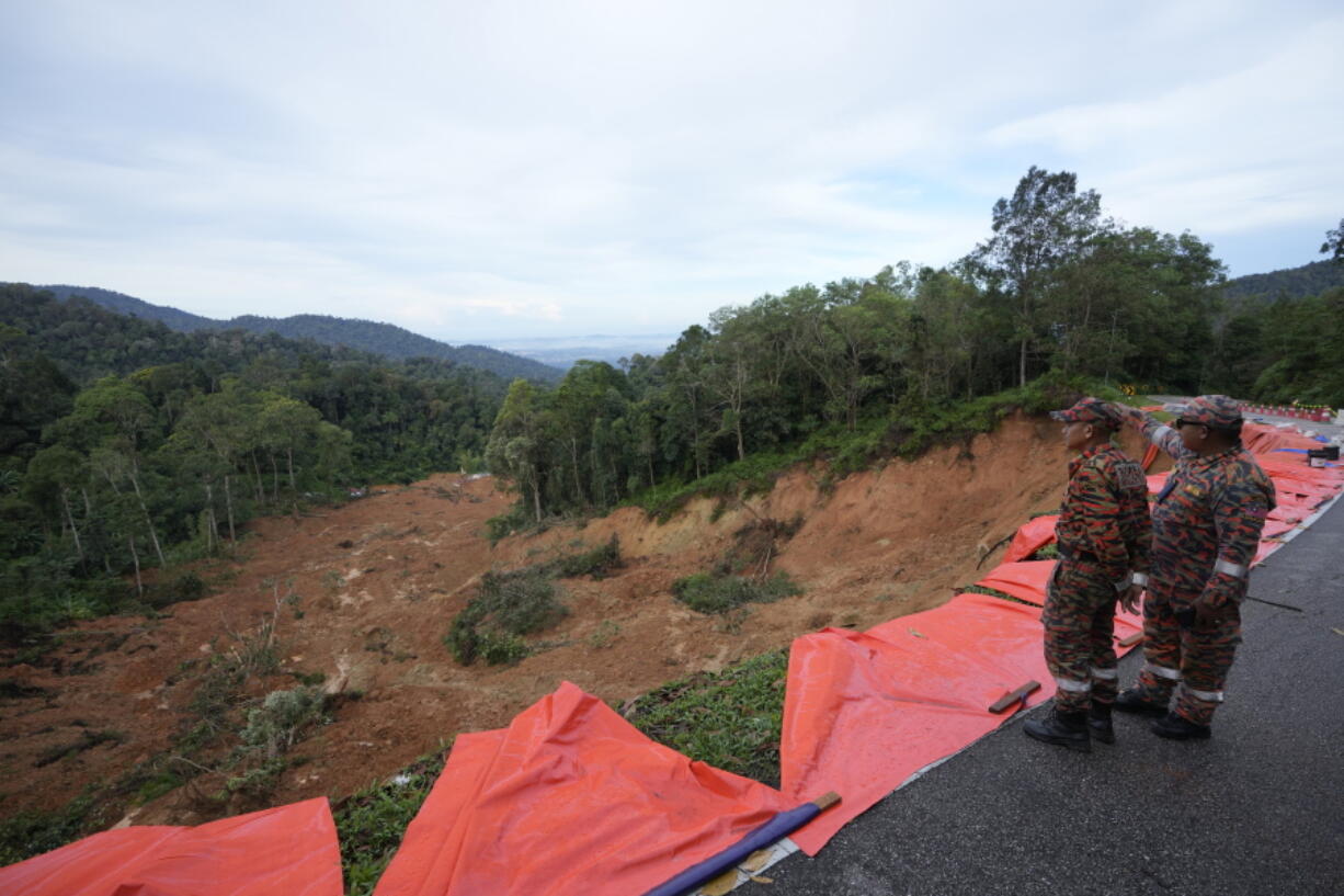 Fire and rescue team members look down on a landslide Saturday, Dec. 17, 2022, in Batang Kali, Malaysia. A landslide Friday, Dec. 16, 2022, at a tourist campground in Malaysia left more than a dozen of people dead and authorities said a dozen of others were feared buried at the site on an organic farm outside the capital of Kuala Lumpur.