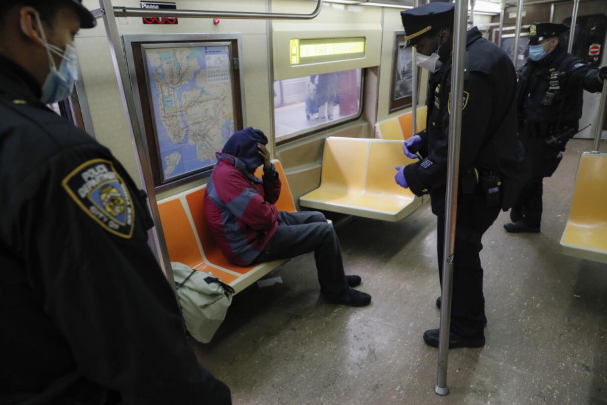 FILE - New York Police Department officers wake up sleeping passengers and direct them to the exits at the 207th Street station on the A train, Thursday, April 30, 2020, in the Manhattan borough of New York. In New York City's latest effort to address a mental health crisis on its streets and subways, Mayor Eric Adams announced Tuesday, Nov. 29, 2022, that authorities would more aggressively intervene to help people in need of treatment, saying there was "a moral obligation" to do so, even if it means providing care to those who don't ask for it.