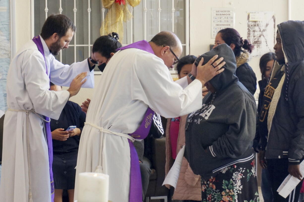 The Rev. Brian Strassburger, left, and the Rev. Flavio Bravo, right, bless migrants during Mass at the Casa del Migrant shelter in Reynosa, Mexico, on Dec. 15, 2022. Both hope and tension have been rising here and the few other shelters in this border city where thousands of migrants await news of U.S. border policy changes possibly less than a week away.