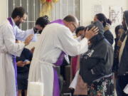 The Rev. Brian Strassburger, left, and the Rev. Flavio Bravo, right, bless migrants during Mass at the Casa del Migrant shelter in Reynosa, Mexico, on Dec. 15, 2022. Both hope and tension have been rising here and the few other shelters in this border city where thousands of migrants await news of U.S. border policy changes possibly less than a week away.