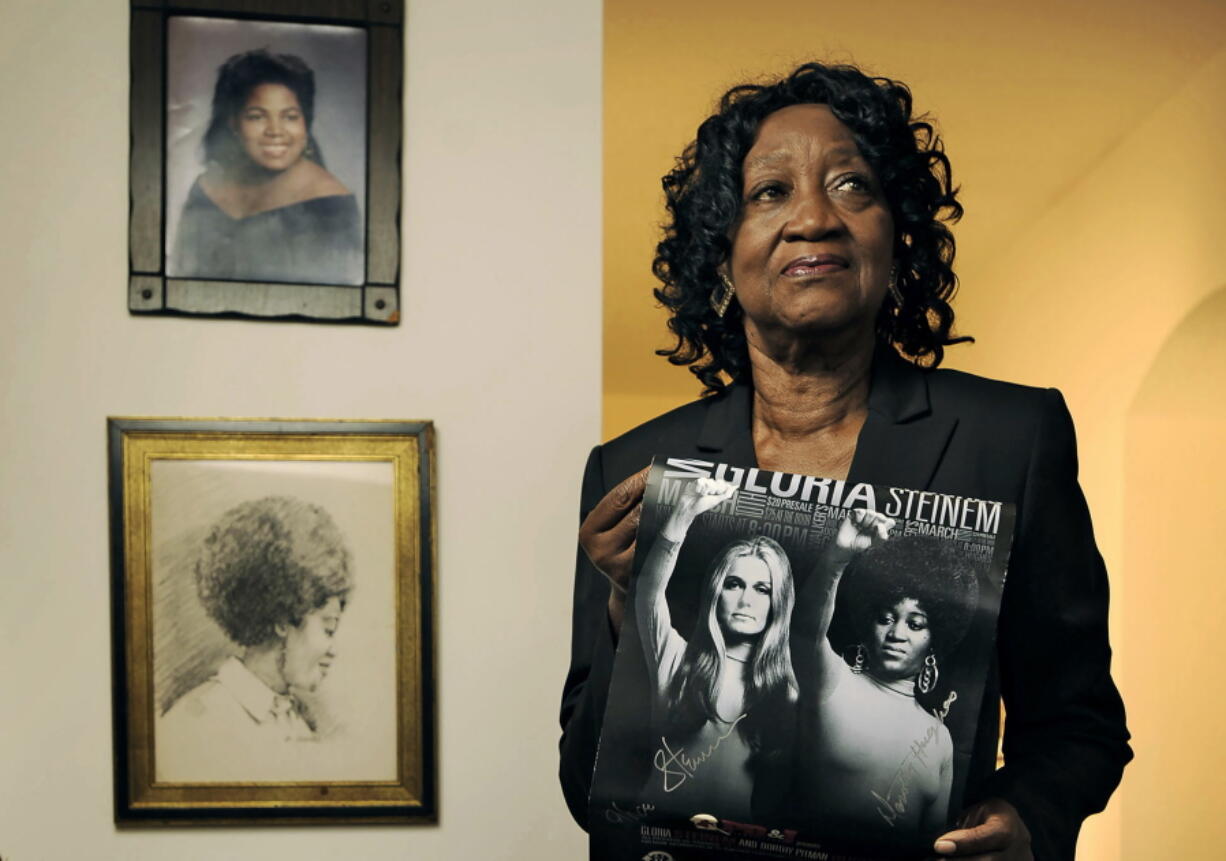 Dorothy Pitman Hughes poses in her St. Johns, Fla., home on Sept.  24, 2013, with a poster using a 1970's image of herself and Gloria Steinem. Hughes, a pioneering Black feminist, child welfare advocate and activist who formed a powerful speaking partnership with Steinem and appeared with her in one of the most iconic photos of the feminist movement, has died. Hughes died Dec. 1, 2022, in Tampa, Fla. She was 84.