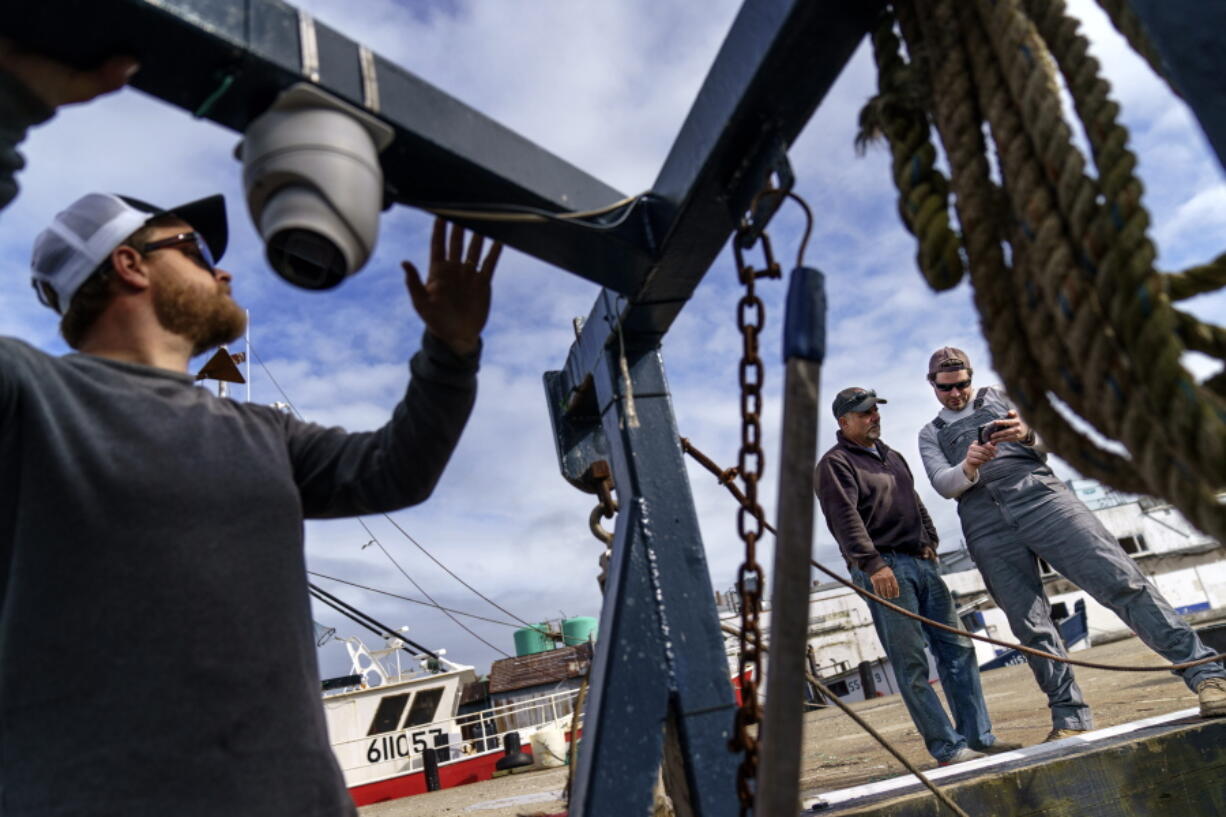 Mark Hager, left, positions a camera with the help of Anthony Lucia, right, as captain Al Cottone watches the feed on a monitor from his boat, the Sabrina Maria, in Gloucester, Mass., May 11, 2022. Hager's Maine-based startup, New England Maritime Monitoring, is one of a bevy of companies seeking to help commercial vessels comply with new federal mandates aimed at protecting dwindling fish stocks. But taking the technology overseas, where the vast majority of seafood consumed in the U.S. is caught, is a steep challenge.