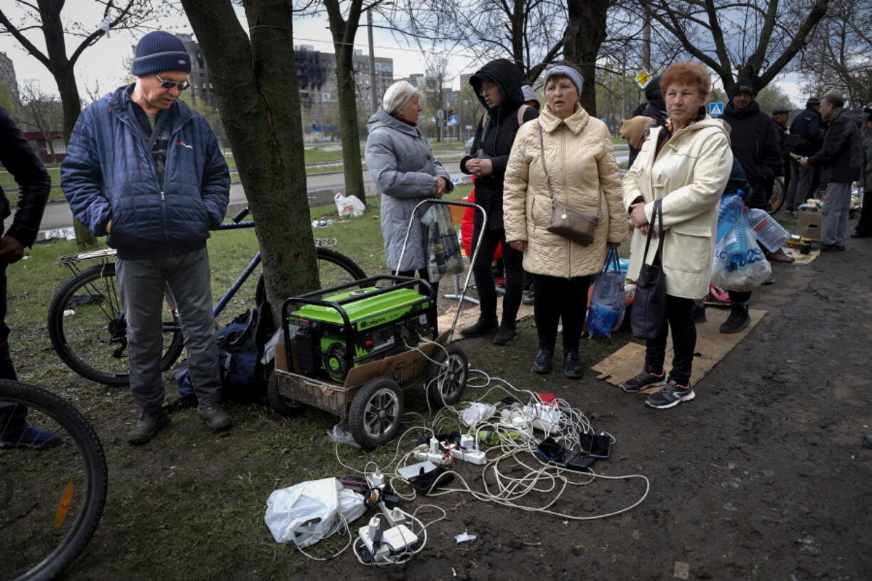 FILE - Local residents gather near a generator to charge their mobile devices in an area controlled by Russian-backed separatist forces in Mariupol, Ukraine, Friday, April 22, 2022. When Russian forces two months ago launched a military campaign against infrastructure in Ukraine, it opened an urgent second front far from the contact line: Along power lines, water mains, and heating systems, and in places like homes, schools, offices and churches.