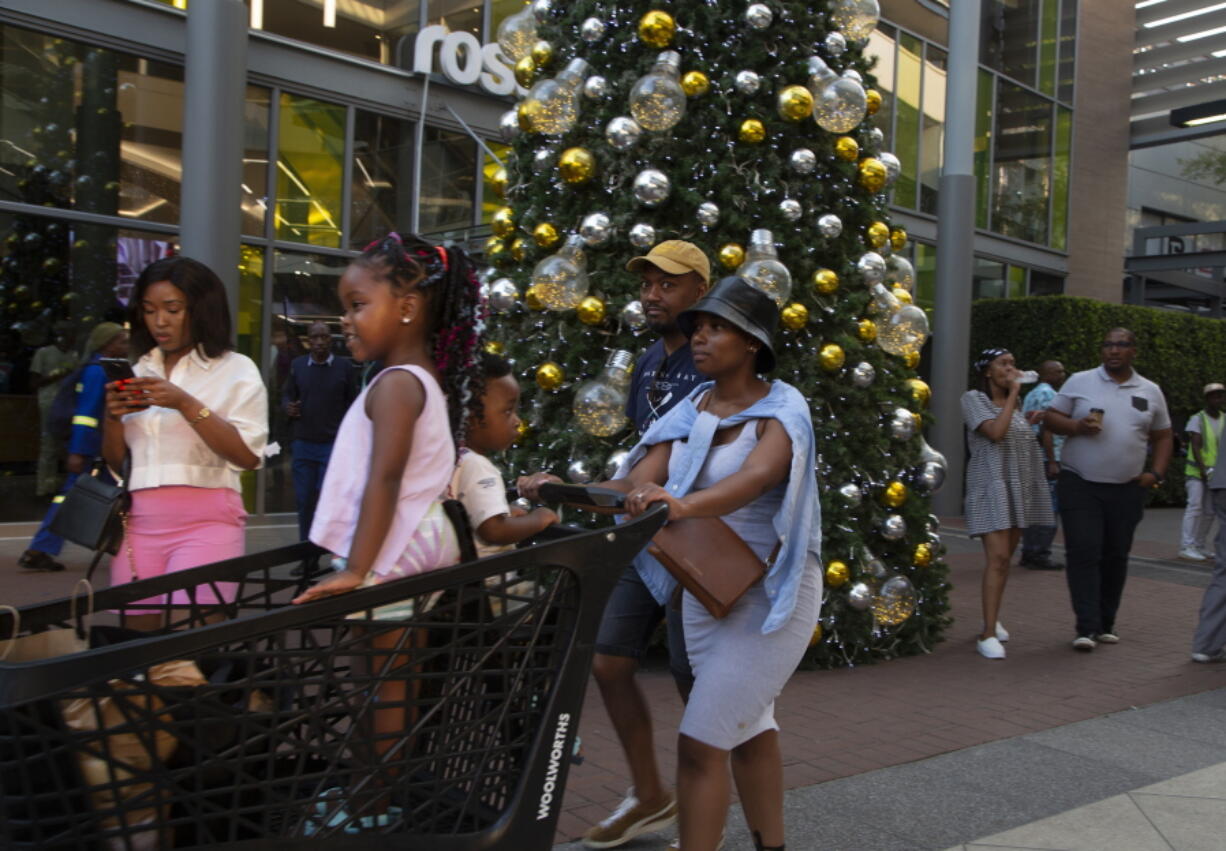 Shoppers pass a Christmas tree at the entrance to the Rosebank Shopping Mall in Johannesburg Saturday, Dec. 23, 2022. South Africa's Christmas 2022 is a start/stop affair because the country's daily power cuts are hitting just about every aspect of the holiday with businesses and families coping with rolling outages of electricity lasting from seven to 10 hours per day.