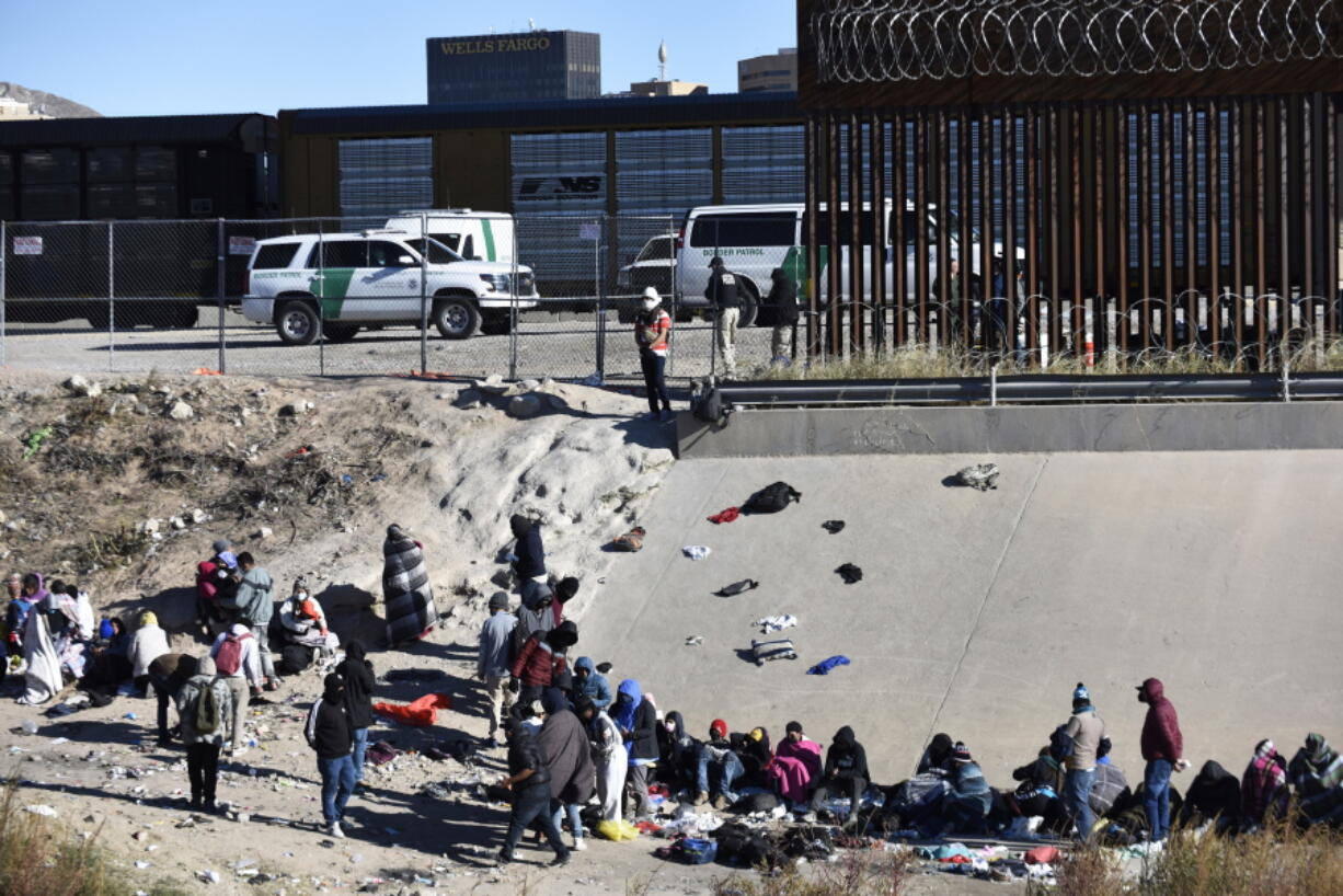 FILE - Migrants wait to cross the U.S.-Mexico border from Ciudad Ju?rez, Mexico, next to U.S. Border Patrol vehicles in El Paso, Texas, Wednesday, Dec. 14, 2022. A federal judge on Thursday temporarily blocked the Biden administration from ending a Trump-era policy requiring asylum-seekers to wait in Mexico for hearings in U.S. immigration court.