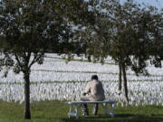 FILE - A visitor sits on a bench to look artist Suzanne Brennan Firstenberg's "In America: Remember," a temporary art installation made up of white flags to commemorate Americans who have died of COVID-19, on the National Mall in Washington on Oct. 2, 2021. The number of U.S. deaths has dropped in 2022 after soaring for two years during the COVID-19 pandemic, but it still is much higher than the levels before the coronavirus hit.