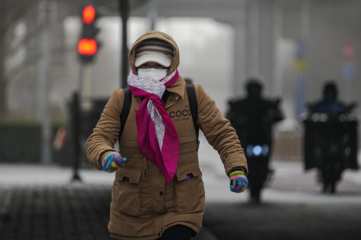 A woman wearing a face mask and covered with hood runs across a street Beijing, Monday, Dec. 12, 2022, as the capital city is hit by sandstorm. China will drop a travel tracing requirement as part of an uncertain exit from its strict "zero-COVID" policies that have elicited widespread dissatisfaction.