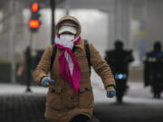 A woman wearing a face mask and covered with hood runs across a street Beijing, Monday, Dec. 12, 2022, as the capital city is hit by sandstorm. China will drop a travel tracing requirement as part of an uncertain exit from its strict "zero-COVID" policies that have elicited widespread dissatisfaction.