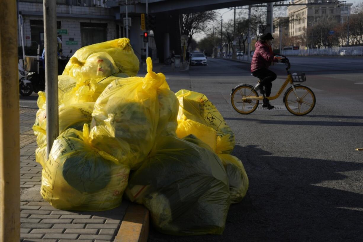 A cyclist passes by household waste inside yellow trash bags marked as medical waste in Beijing, Wednesday, Dec. 7, 2022. In a sharp reversal, China has announced a series of measures rolling back some of the most draconian anti-COVID-19 restrictions.