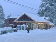 A person shovels snow outside Rome Grocery northeast of Bellingham, Wash., on Tuesday morning, Dec. 20, 2022. Heavy snow, freezing rain and sleet have disrupted travel across the Pacific Northwest, causing widespread flight cancellations and creating hazardous driving conditions.