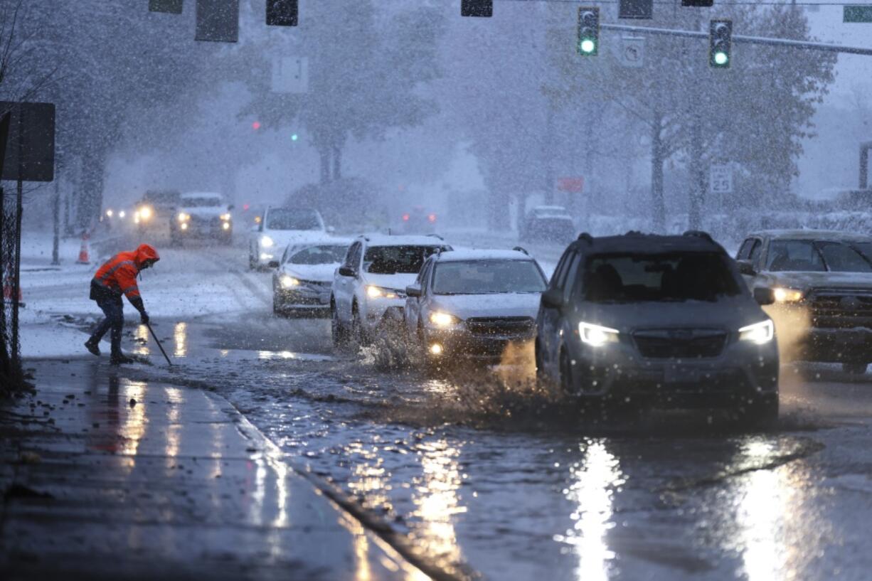 A worker from Washington Department of Transportation clears a drain on Northgate Way during a heavy snow at the morning commute in Seattle, on Tuesday, Dec. 20, 2022.