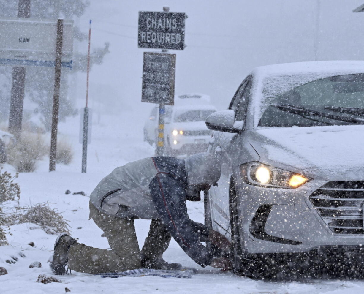 Evan Freedman, from Los Angeles, puts snow chains on his vehicle as heavy snow falls on Highway 2 near Wrightwood, Calif., on Monday, Dec. 12, 2022.