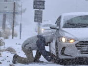 Evan Freedman, from Los Angeles, puts snow chains on his vehicle as heavy snow falls on Highway 2 near Wrightwood, Calif., on Monday, Dec. 12, 2022.