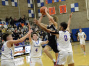 Woodland’s Beau Swett (1) drives between Ridgefield’s Cole Chester (4), Colten Castro (10) and Sid Bryant (0) during a game at Ridgefield High School on Wednesday, Jan.