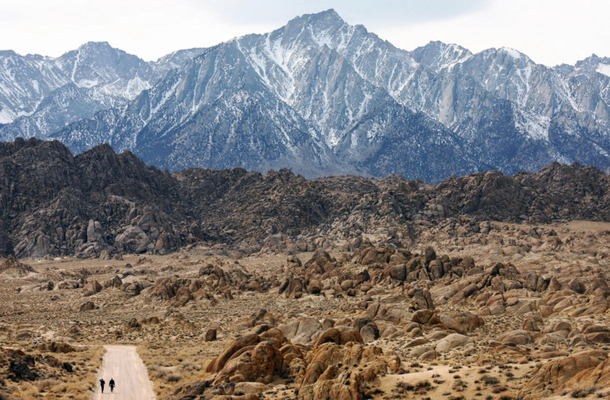 In this photo from February 20, 2022, film crew workers walk through the Alabama Hills beneath the lightly snow-capped Sierra Nevada Mountains (TOP) near Lone Pine, California.