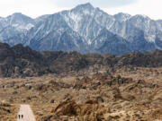 In this photo from February 20, 2022, film crew workers walk through the Alabama Hills beneath the lightly snow-capped Sierra Nevada Mountains (TOP) near Lone Pine, California.