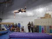 Reese Velansky of Washougal High School dismounts from the balance beam as Camas coaches and gymnasts look on during a meet at Naydenov Gymnastics on Dec. 17.