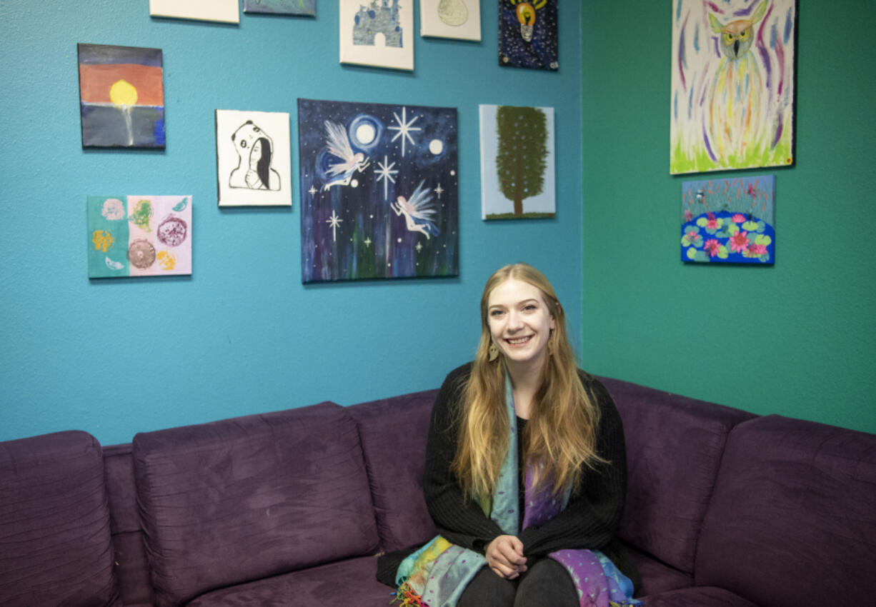 Youth House staff member Maranda Heckler sits for a portrait below artwork created by clients who are part of the Options or Healthy Transitions programs at Clark County Youth House. Heckler is a case manager and a certified peer counselor with the Healthy Transitions Program, where she uses her own lived experience to offer support to youth struggling with their mental health.