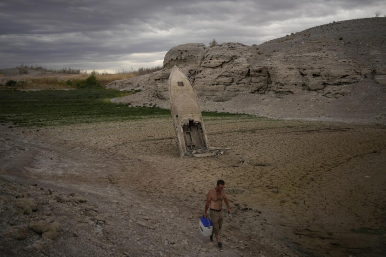 FILE - A man walks by a formerly sunken boat standing upright into the air with its stern buried in the mud along the shoreline of Lake Mead amid a drought at the Lake Mead National Recreation Area near Boulder City, Nev., June 22, 2022. Costly weather disasters kept raining down on America last year, pounding the nation with 18 climate extremes that caused at least $1 billion in damage each, totaling more than $165 billion, federal climate scientists calculated Tuesday, Jan. 10, 2023.