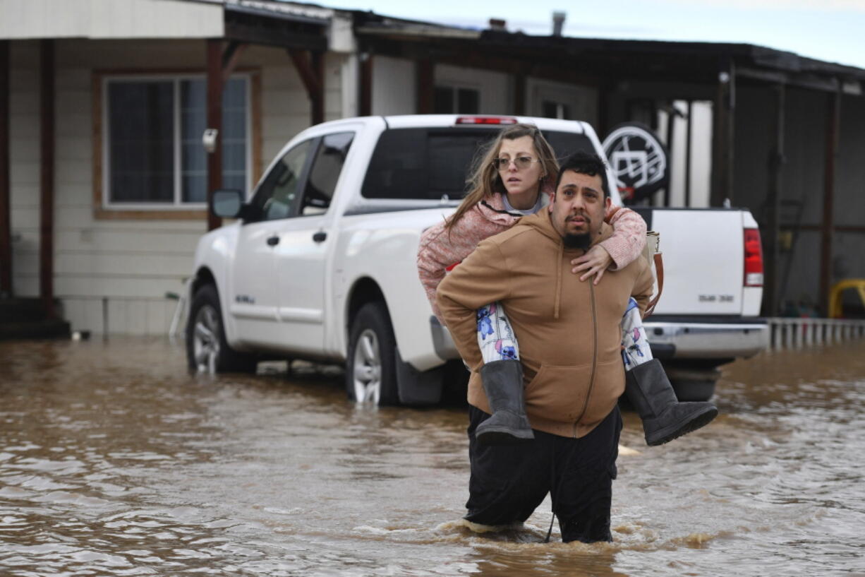 Ryan Orosco, of Brentwood, carries his wife Amanda Orosco, from their flooded home on Bixler Road in Brentwood, Calif., on Monday, Jan. 16, 2023. The last in a three-week series of major winter storms is churning through California.