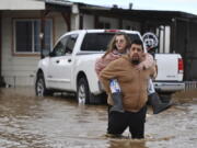 Ryan Orosco, of Brentwood, carries his wife Amanda Orosco, from their flooded home on Bixler Road in Brentwood, Calif., on Monday, Jan. 16, 2023. The last in a three-week series of major winter storms is churning through California.