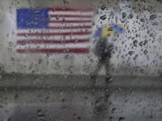 FILE - A pedestrian carries an umbrella while walking past a painting of an American flag in San Francisco, Jan. 11, 2023. A new study says the drenching that California has been getting since Christmas will only get wetter and nastier with climate change.