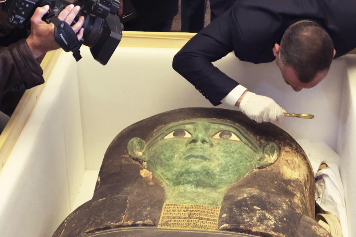 Mostafa Waziri, top official at the Supreme Council of Antiquities, takes a look with a magnifier at an ancient wooden sarcophagus during a handover ceremony at the foreign ministry in Cairo, Egypt, Monday, Jan. 2, 2023. An ancient wooden sarcophagus that was featured at the Houston Museum of Natural Sciences was returned to Egypt after U.S. authorities determined it was looted years ago, Egyptian officials said Monday.