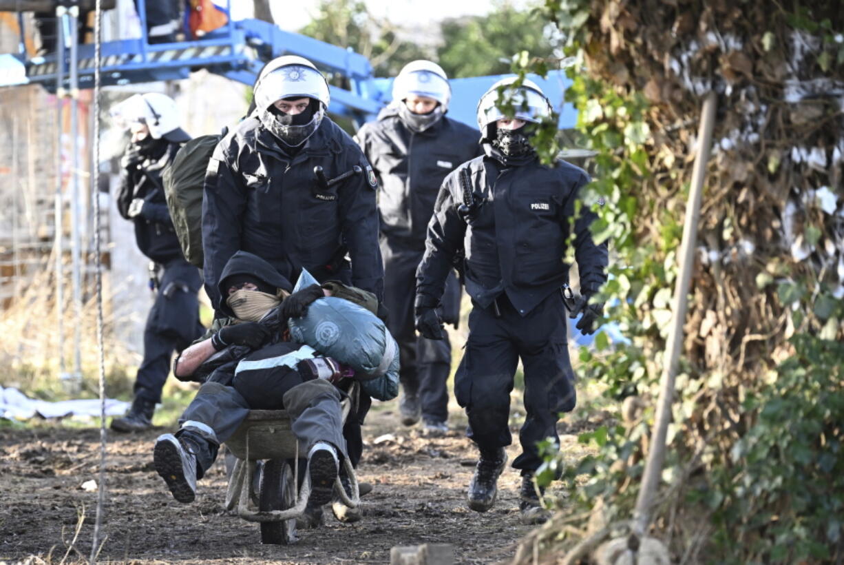 Police officers push a climate activist with a wheelbarrow off the site in the village Luetzerath in Erkelenz, Germany, Sunday, Jan. 15, 2023. The energy company RWE wants to excavate the coal lying under Luetzerath, for this purpose, the hamlet on the territory of the city of Erkelenz at the opencast lignite mine Garzweiler II is to be demolished.