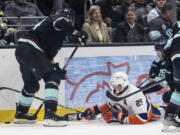 New York Islanders forward Brock Nelson, center, fights for the puck against Seattle Kraken defenseman Jamie Oleksiak, left, and forward Jared McCann after getting knocked to the ice during the third period of an NHL hockey game, Sunday, Jan. 1, 2023, in Seattle. The Kraken won 4-1.