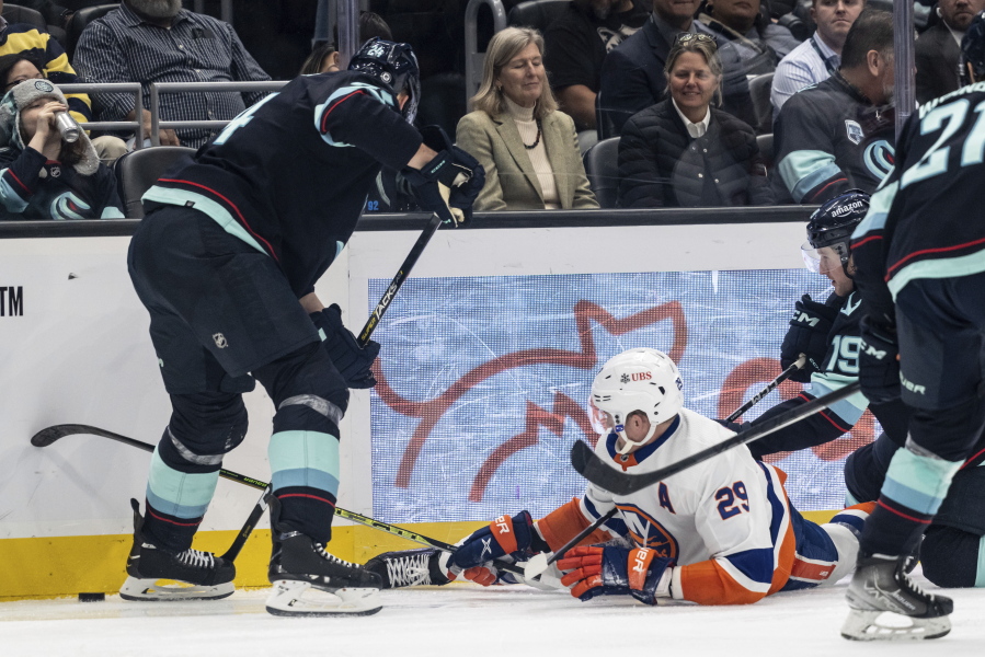 New York Islanders forward Brock Nelson, center, fights for the puck against Seattle Kraken defenseman Jamie Oleksiak, left, and forward Jared McCann after getting knocked to the ice during the third period of an NHL hockey game, Sunday, Jan. 1, 2023, in Seattle. The Kraken won 4-1.