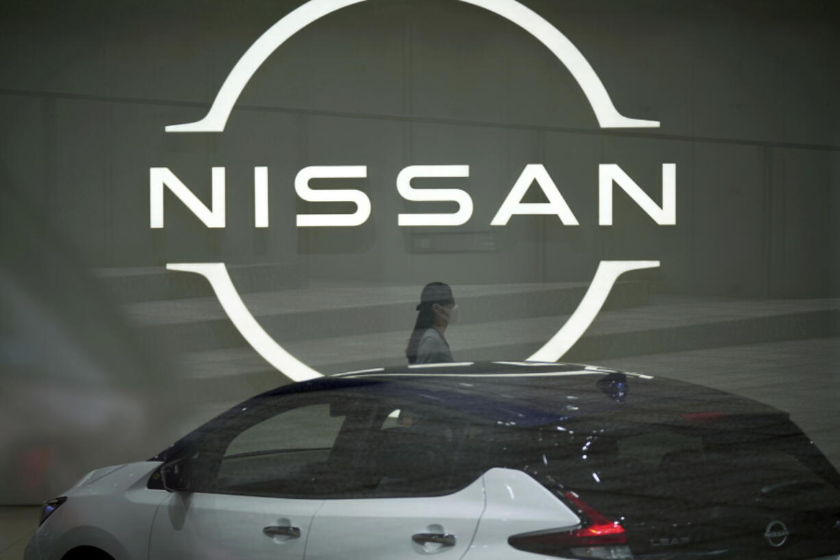 FILE - A staff walking near a Nissan logo at Nissan headquarters is seen though a window on May 12, 2022, in Yokohama near Tokyo. Nissan and Renault have changed their mutual cross-shareholdings to the same 15%, ironing out a source of conflict in the Japan-French auto alliance.