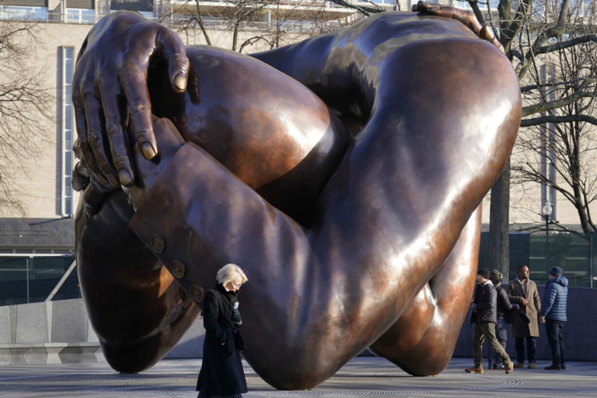 Passers-by walk near the 20-foot-high bronze sculpture "The Embrace," a memorial to Dr. Martin Luther King Jr. and Coretta Scott King, in the Boston Common, Tuesday, Jan. 10, 2023, in Boston. The sculpture, consisting of four intertwined arms, was inspired by a photo of the Kings embracing when MLK learned he had won the Nobel Peace Prize in 1964. The statue is to be unveiled during ceremonies Friday, Jan. 13, 2023.