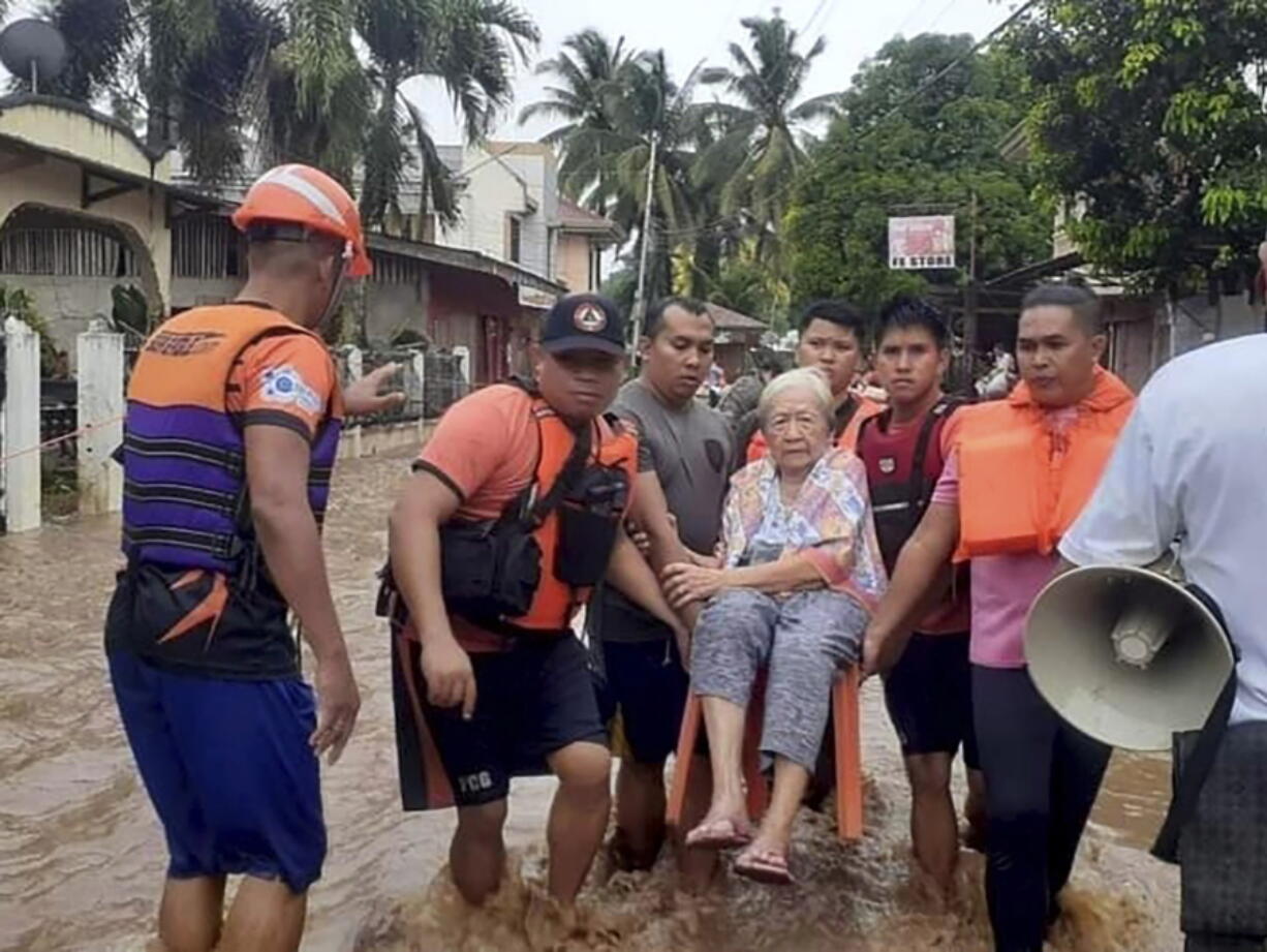 In this image provided by the Philippine Coast Guard, an elderly woman sits on a chair while being carried by coast guard personnel wading through floodwaters in Plaridel, Misamis Occidental province in the southern Philippines, Monday, Dec. 26, 2022. Heavy rains and floods devastated parts of the Philippines over the Christmas weekend.