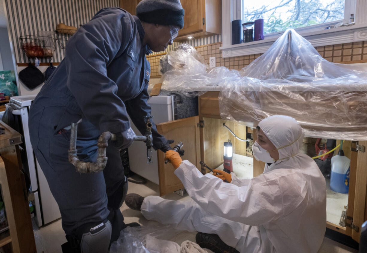 Tonya Miller (l), an apprentice plumber with Harts Services, takes a piece of galvanized pipe that apprentice Ricky Bui, who has been in the field longer than Miller, has just cut from beneath the kitchen sink of a Des Moines, Washington, home Wednesday, January 4, 2023. The apprentices are working to replace the old galvanized water system in the home with upgraded plastic pex water lines. (Ellen M.