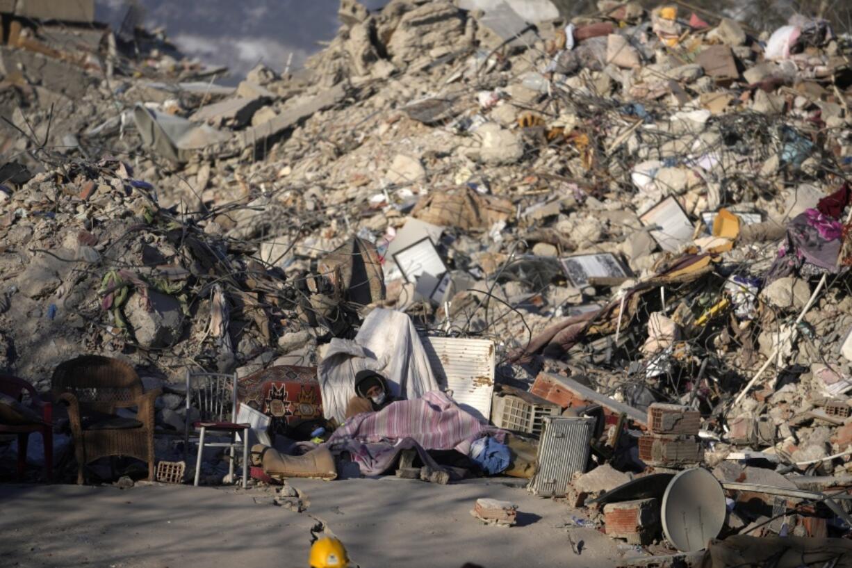 A man sleeps in front of a destroyed building in Kahramanmaras, southeastern Turkey, Monday, Feb. 13, 2023. Thousands left homeless by a massive earthquake that struck Turkey and Syria a week ago packed into crowded tents or lined up in the streets for hot meals Monday, while the desperate search for anyone still alive likely entered its last hours.