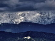 Storm clouds and snow are seen over the San Gabriel mountain range behind Griffith Observatory in the Hollywood Hills part of Los Angeles on Sunday, Feb. 26, 2023. A powerful winter storm that swept the West Coast with flooding and frigid temperatures has shifted to southern California, swelling rivers to dangerous levels and dropping snow in even low-lying areas around Los Angeles.