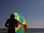 FILE - A man folds his umbrella on the beach Tuesday, Aug. 7, 2018, in Laguna Beach, Calif. Environmental advocates are celebrating in Laguna Beach -- but it won't be with balloons. The hilly, seaside city is weighing a plan to ban the sale and public use of balloons to curtail the risk of devastating wildfires and eliminate a major source of trash floating near the community's scenic shores. (AP Photo/Jae C.