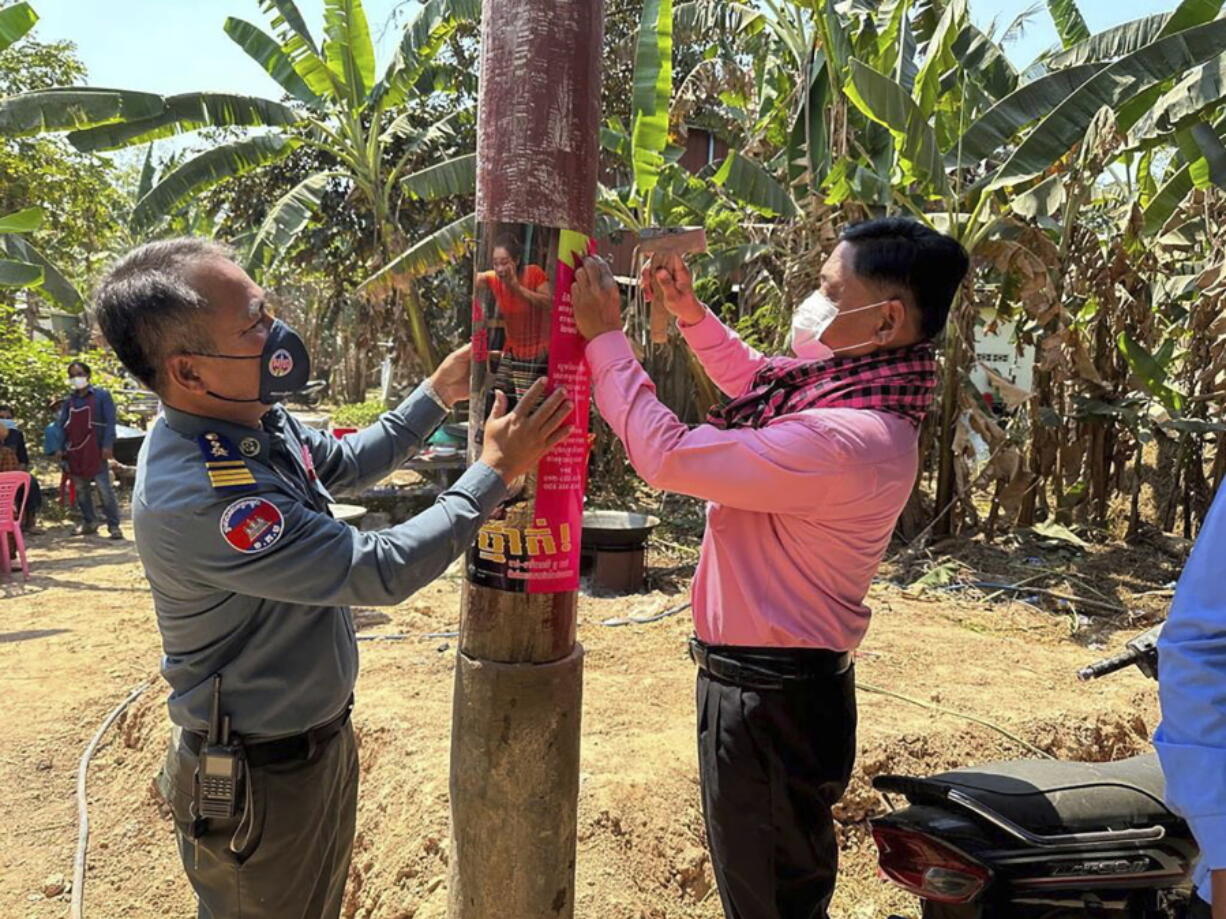 In this photo released by the Cambodia Ministry of Health, a Cambodia animal health officer, right, and a military police officer place posters about awareness of H5N1 virus threats in hopes of educating villagers to take care of their health, in Prey Veng eastern province Cambodia, Thursday, Feb. 23, 2023. An 11-year-old girl in Cambodia has died from bird flu in the country's first known human H5N1 infection since 2014, health officials said.