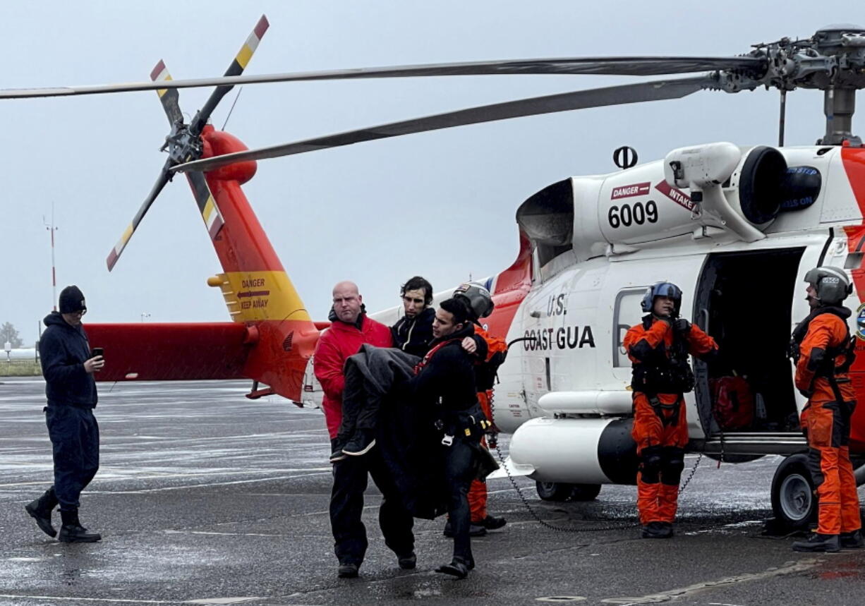 In this photo provided by the U.S Coast Guard Pacific Northwest, Coast Guard personnel help carry a swimmer from a rescue helicopter after he was rescued from the mouth of the Columbia River after his boat was capsized by a giant wave on Friday, Feb. 3, 2023, at Coast Guard Base Astoria, Ore. A newly minted Coast Guard rescue swimmer saved the man's life at the mouth of the river between Oregon and Washington state. (AET1 Kyle Turcotte/U.S.