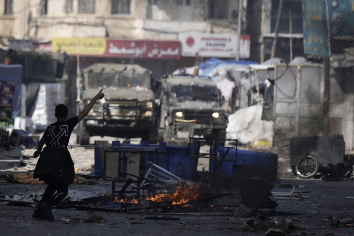 A Palestinian gestures to Israeli military vehicles during clashes in the West Bank city of Nablus, Wednesday, Feb. 22, 2023. Israeli troops moved into the city, setting off fighting that killed several Palestinians, including a 72-year-old man, Palestinian health officials said. The Israeli military gave few details about its operation in the northern city, which is known as a militant stronghold, and the army frequently operates there.