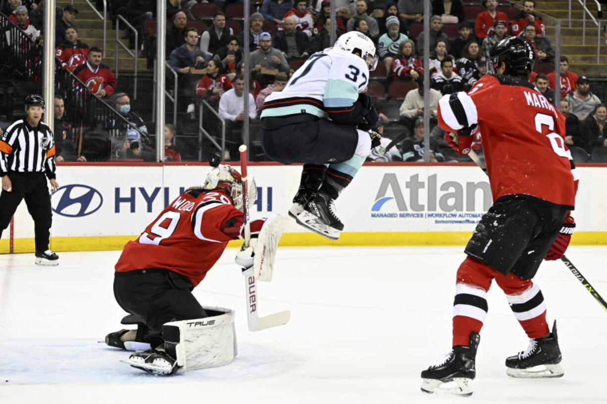 Seattle Kraken center Yanni Gourde (37) jumps as New Jersey Devils goaltender Mackenzie Blackwood (29) has the puck go over his head during the first period of an NHL hockey game Thursday, Feb. 9, 2023, in Newark, N.J.