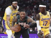 Portland Trail Blazers guard Damian Lillard, center, drives to the basket against Los Angeles Lakers forward Anthony Davis, left, and guard Dennis Schroder, right, during the first half of an NBA basketball game in Portland, Ore., Monday, Feb. 13, 2023.