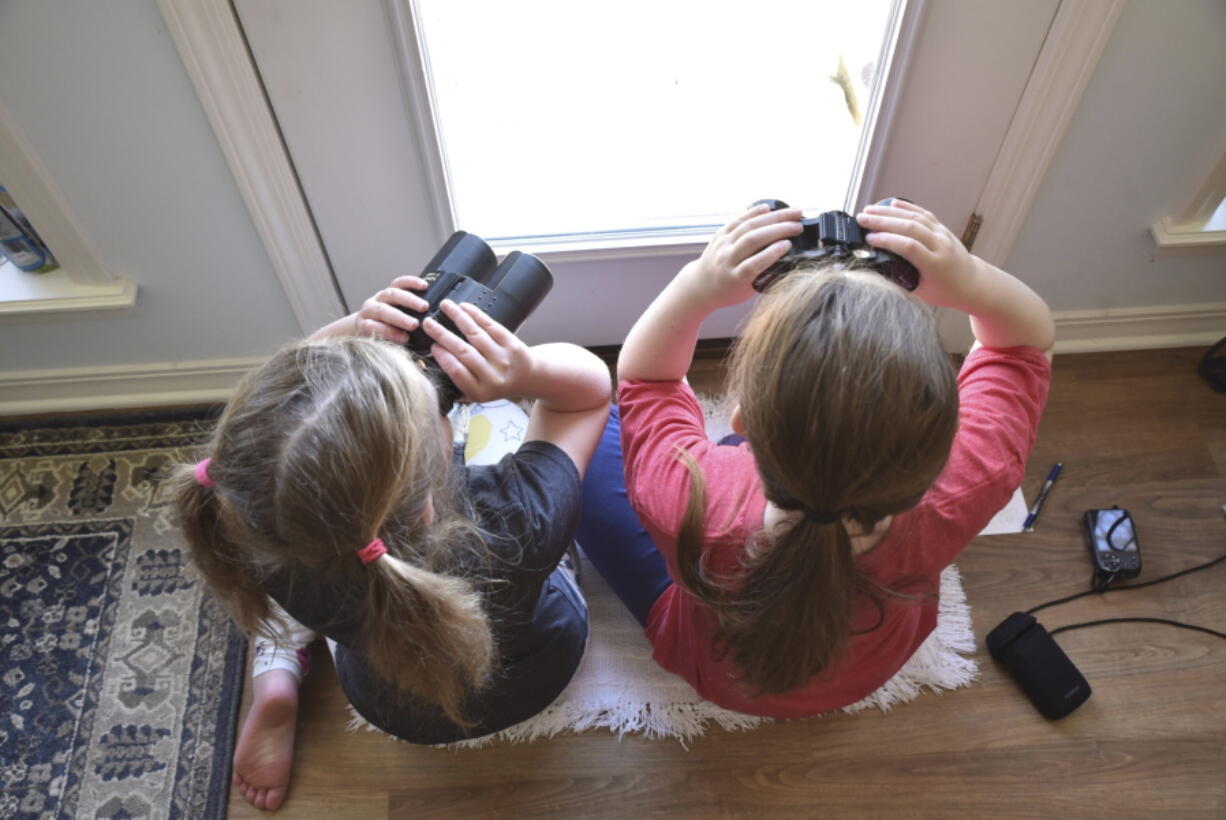 Two girls watching birds through a window with binoculars, bird lists and cameras in Elm Grove, La., during the Great Backyard Bird Count in February 2022. About 385,000 people from 192 countries took part in the 2022 count, and their results have been used by scientists to study bird populations worldwide.