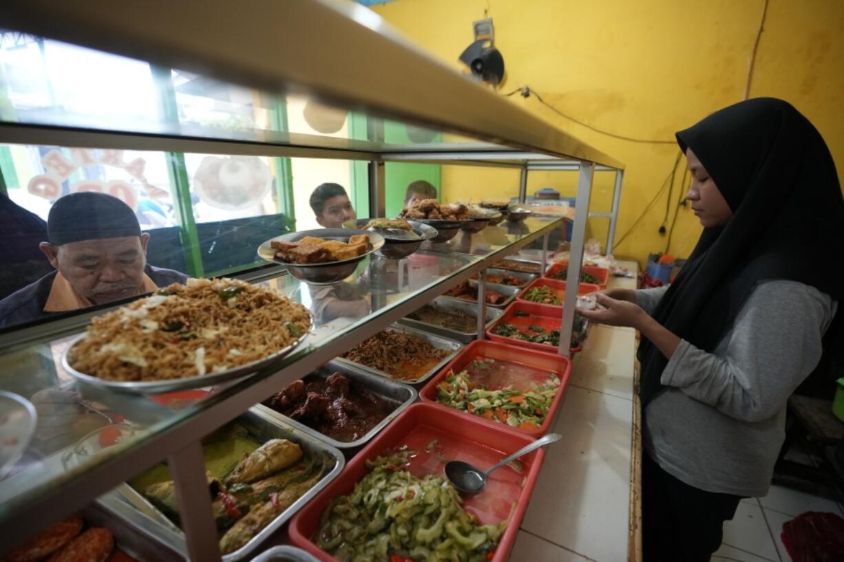 A worker serves customers at a food stall in Bekasi, on the outskirts of Jakarta, Indonesia, Thursday, Feb 2, 2023. Nearly a year after Russia invaded Ukraine, punishingly high food prices are inflicting particular hardship on the world's poor.  In Jakarta, vendors know they can't pass along surging food prices to their already struggling customers.