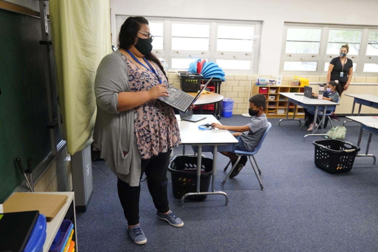 FILE - Teacher Jessica Flores directs students as they work on laptops in a classroom in Newlon Elementary School on, Aug. 25, 2020, in Denver, Colo., which is one of 55 Discovery Link sites set up by Denver Public Schools where students are participating in remote learning during the COVID-19 pandemic. Colorado lawmakers are considering joining eight other states in an agreement that would eliminate many of the requirements for teachers to get licensed when they move within the member states.