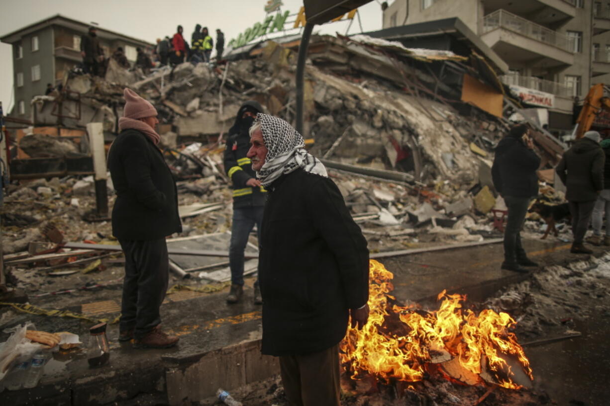 FILE - People warm themselves next to a collapsed building in Malatya, Turkey, on Feb. 7, 2023. A magnitude 5.6 earthquake shook southern Turkey on Monday Feb. 27, 2023 three weeks after a catastrophic temblor devastated the region, causing some already damaged buildings to collapse and killing at least one person, the country's disaster management agency, AFAD, said.